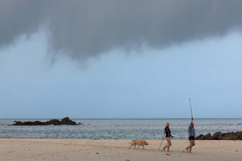 Zwei Spaziergänger mit Stöcke und Hund am Strand in die Bretagne