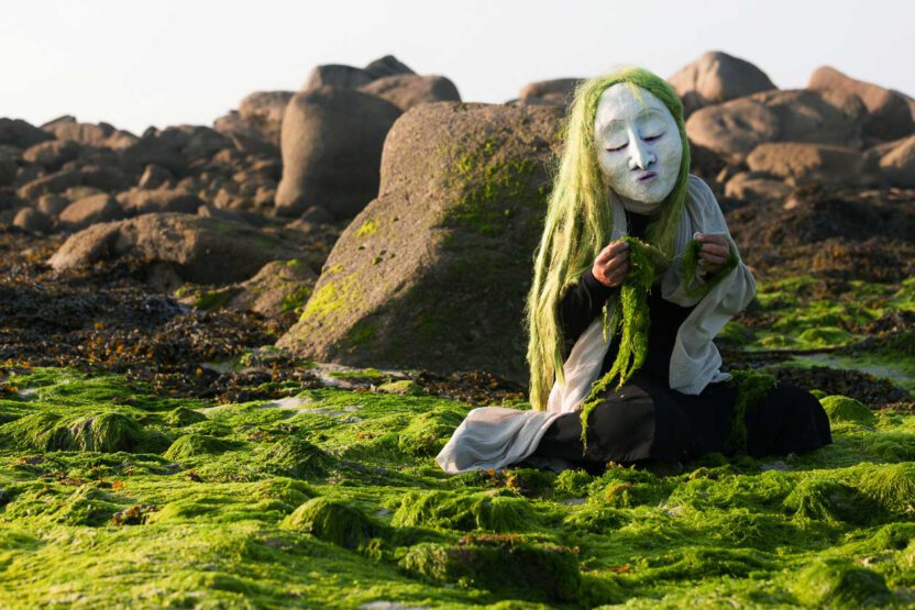 Maskenfigur am Strand mit grüne Algen