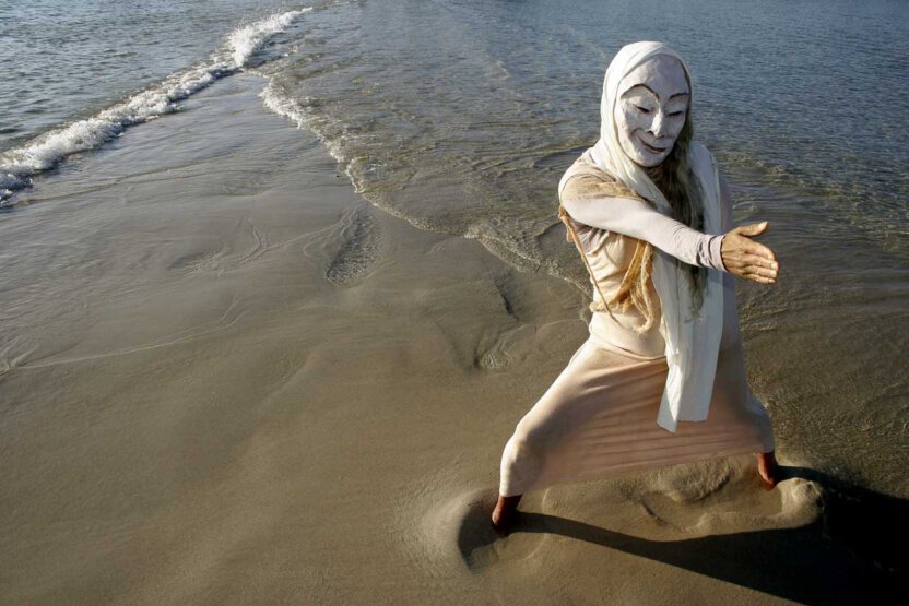 Maskenfigur am Strand mit Wellen
