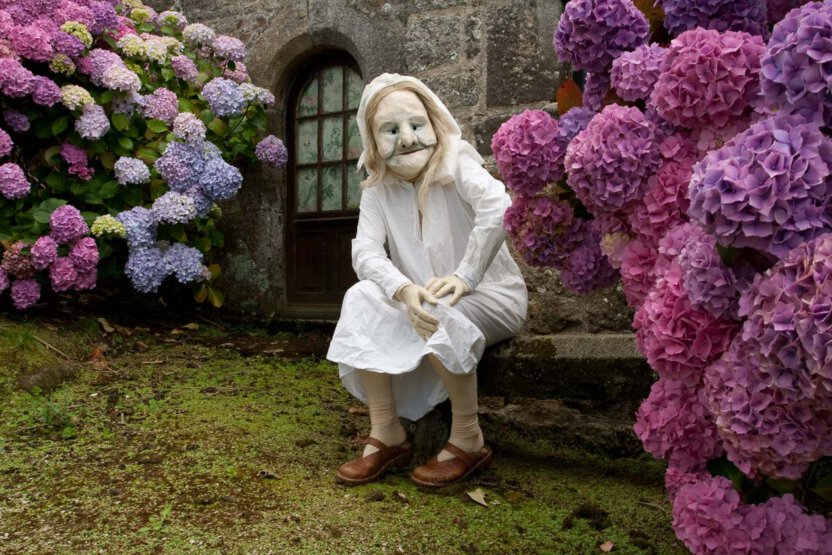 Maskenfigur sitzend zwischen Hortensien in der Bretagne